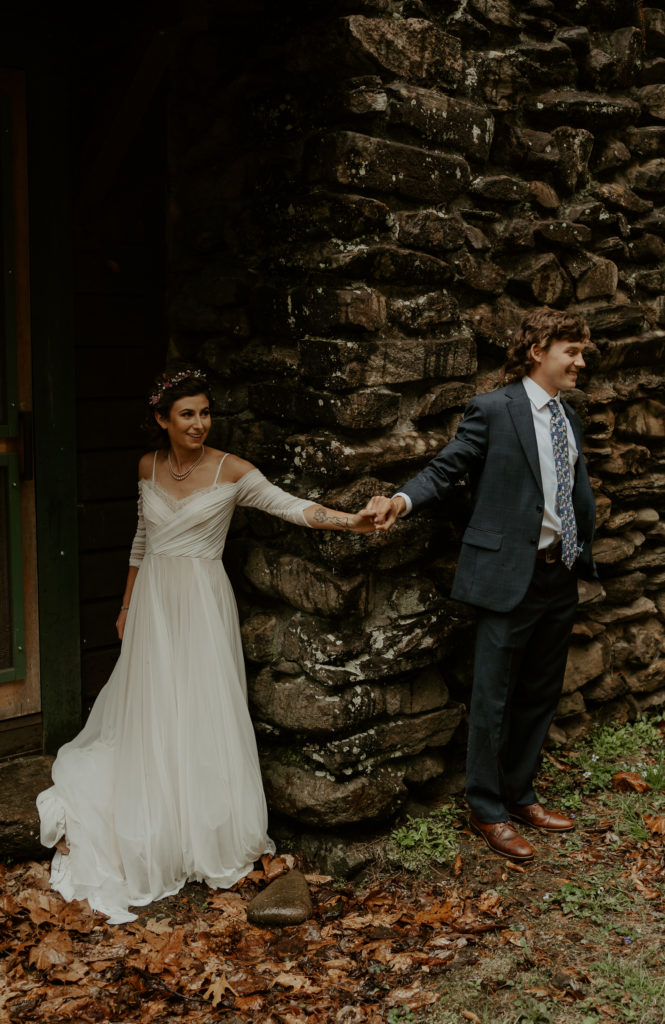A bride and groom holding hands but not seeing each other for their first touch before they get married on their Asheville mountain wedding. 
