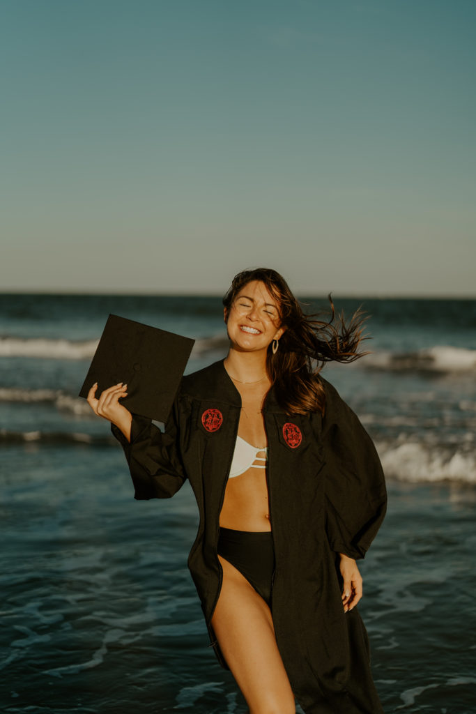 A girl with her cap and gown and a bathing suit on in the ocean for her Charleston graduation photos.