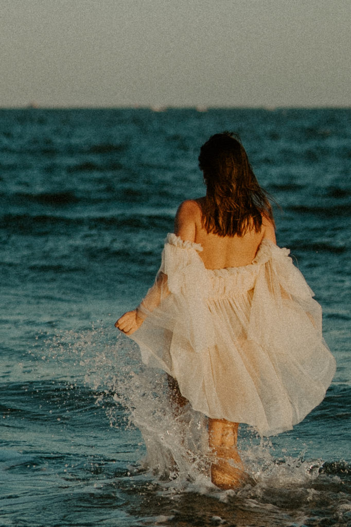 A girl in a dress walking into the ocean for her Charleston graduation photos. 