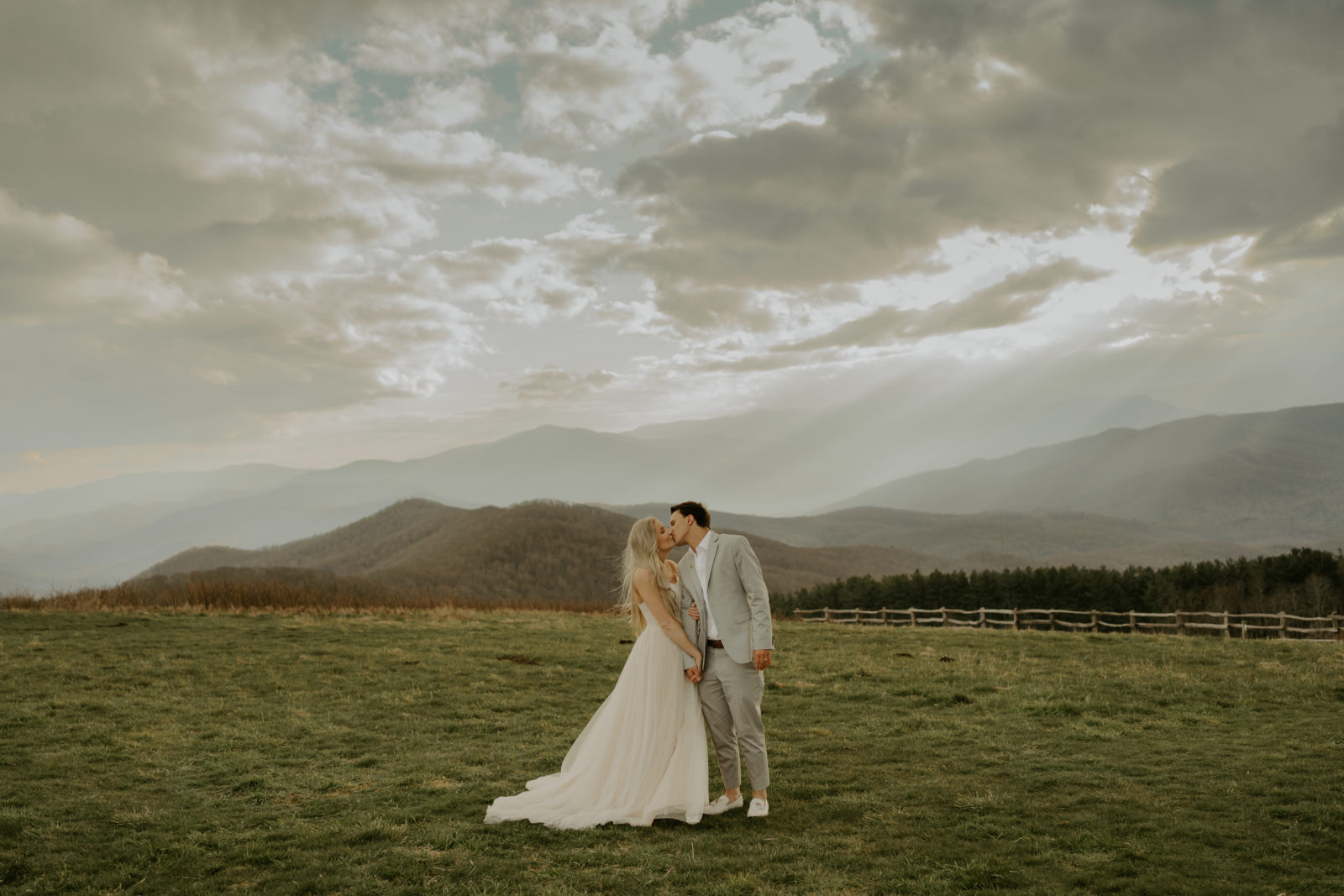 A couple is kissing with their wedding attire on and mountains in the background during their Asheville mountain elopement.