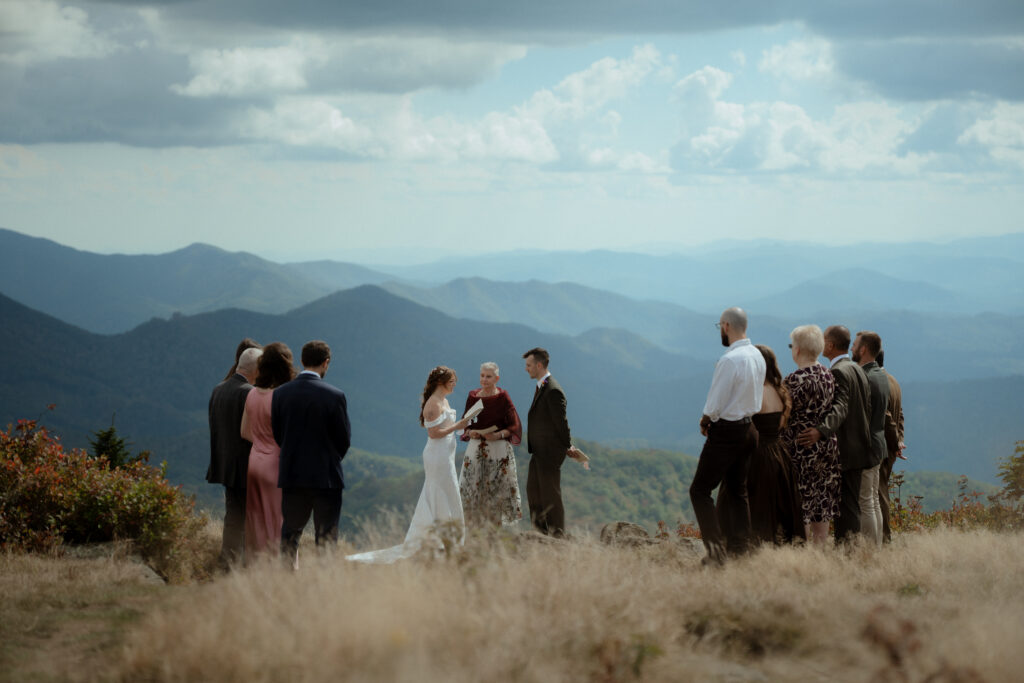 A micro-wedding on Roan mountain with the couple exchanging vows, surrounded by their loved ones and the Blue Ridge mountains behind them.