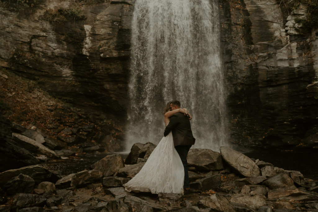 Bride and groom hugging in front of a waterfall after getting married