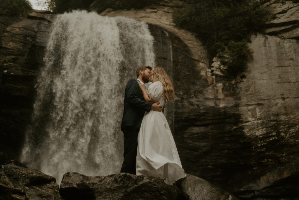 An photo of a man and a woman doing an Asheville engagement photo session with a waterfall in the background