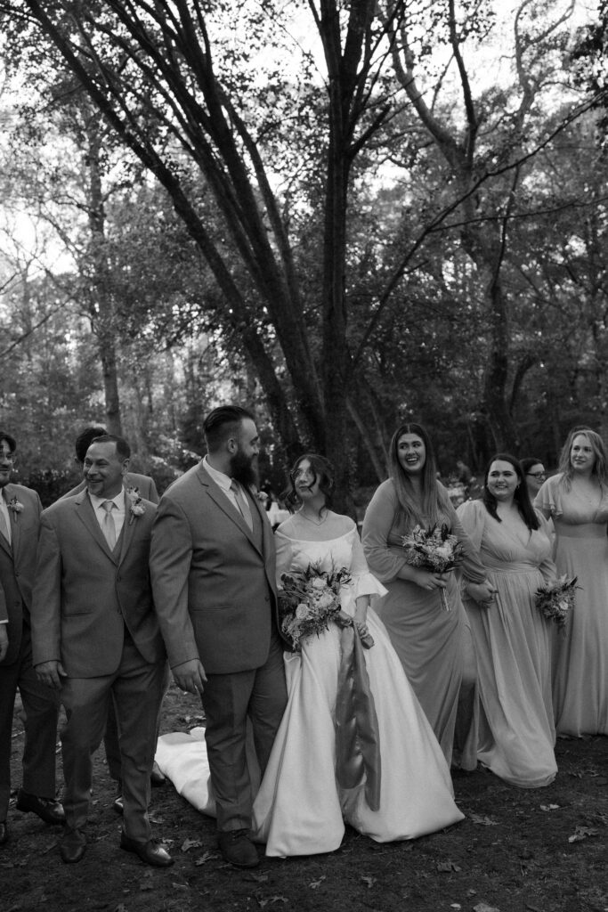 A couple walks with their wedding party through a tree-lined path in North Carolina, celebrating their special day in a scenic outdoor setting.