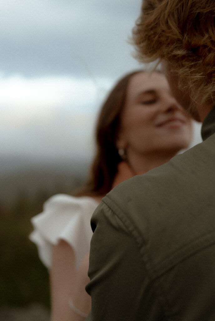 Close-up of a couple as the man gently holds the woman’s face, creating an intimate and tender moment. The texture of his dark green button-up shirt is visible, along with the delicate earrings she is wearing, adding subtle details to the romantic shot.