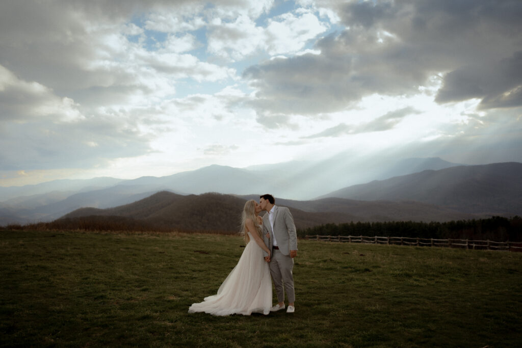 couple getting married on top of Max Patch near Asheville, North Carolina with sun rays going through the clouds in the background.