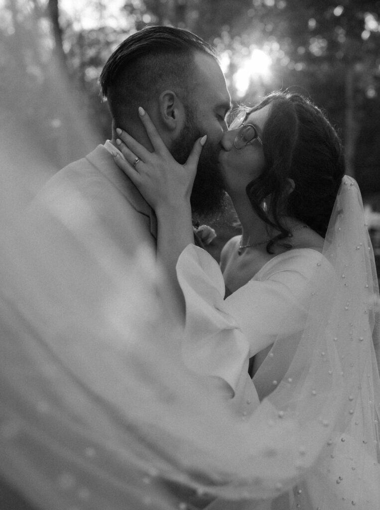 black and white portrait of a couple in wedding attire sharing a kiss, capturing a timeless and intimate moment.