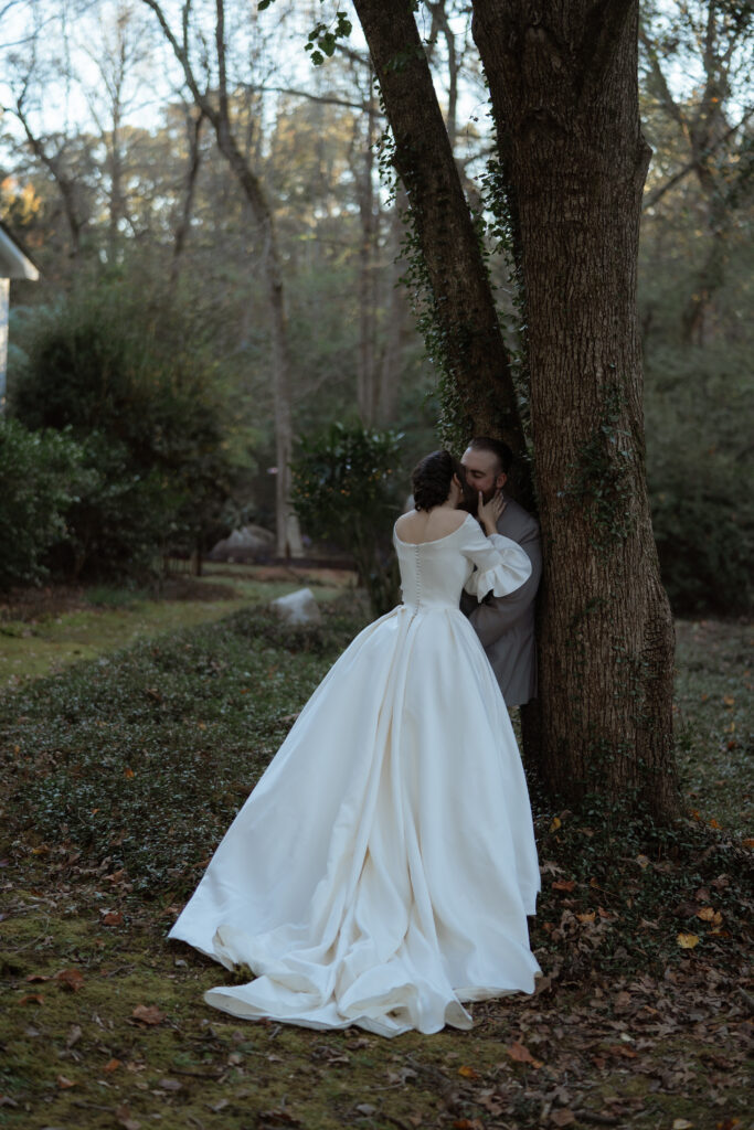 A couple shares a kiss beneath a tree during a luxurious backyard wedding in North Carolina, blending elegance with an intimate setting.