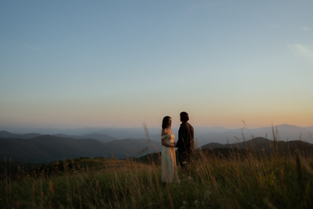 Bride and groom gaze at each other during a romantic summer elopement on Max Patch, surrounded by tall grass and breathtaking mountain views at sunset in Asheville, North Carolina.