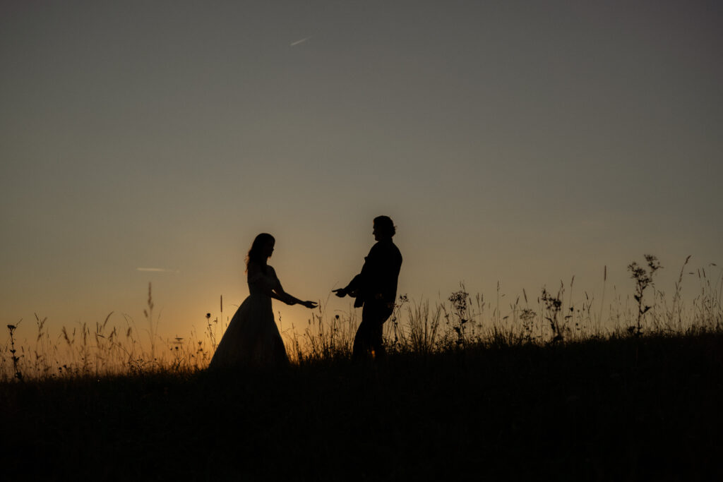 Silhouetted couple stands atop Max Patch Mountain in North Carolina, framed by a glowing sunset over the rolling peaks.