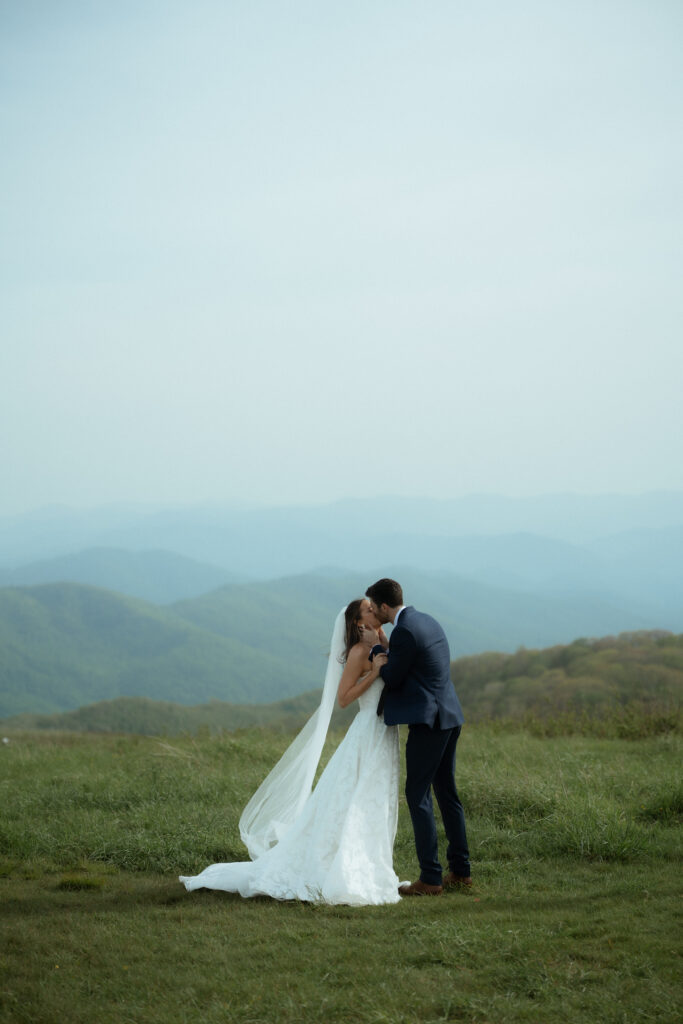 A married couple sharing their first kiss in the mountains near Asheville, North Carolina surrounded by greenery and rolling hills